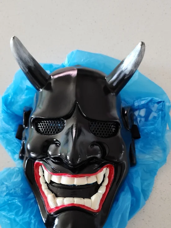 Glossy black Japanese Hannya mask featuring menacing white teeth, red accents
