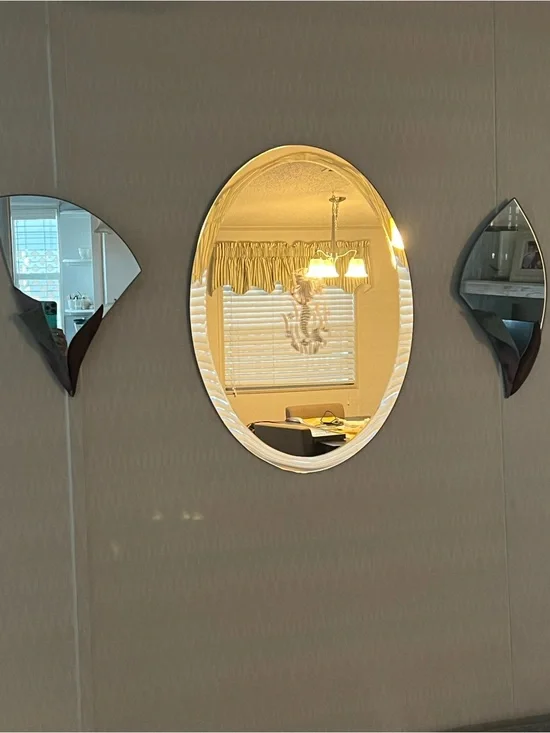 A frameless oval mirror with a mermaid etching with 2 matching mirrored sconces