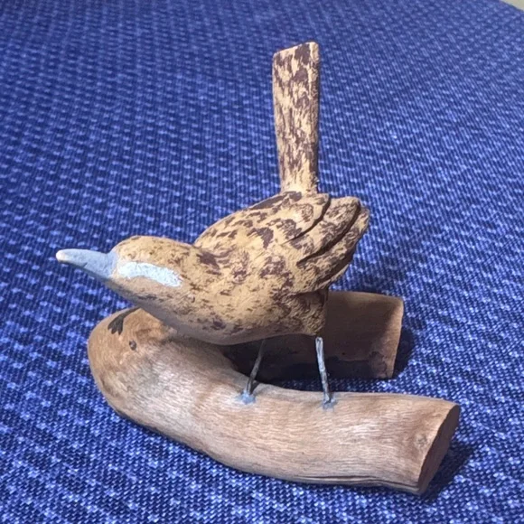 Hand carved wooden bird sculpture perched on a piece of natural wood signed