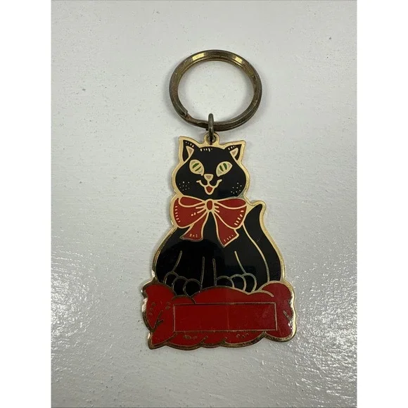 Black cat enamel keychain with gold-toned metal accents and a red bow