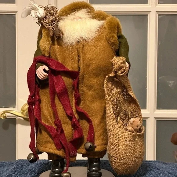 Shaggy haired and bearded Santa wears a brown cape and carries a burlap sack.