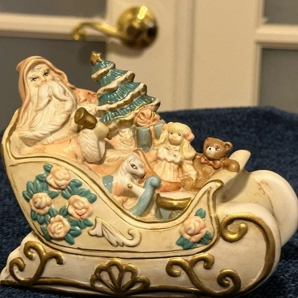 Porcelain musical sleigh holds Santa & gifts. Plays Here Comes Santa Claus.