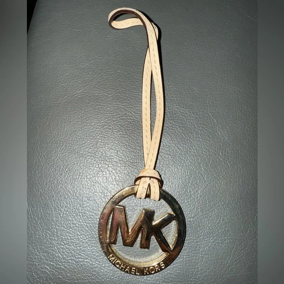 Michael Kors Gold Tone MK Logo Charm With A Light Tan/Creme Color Leather Tassel