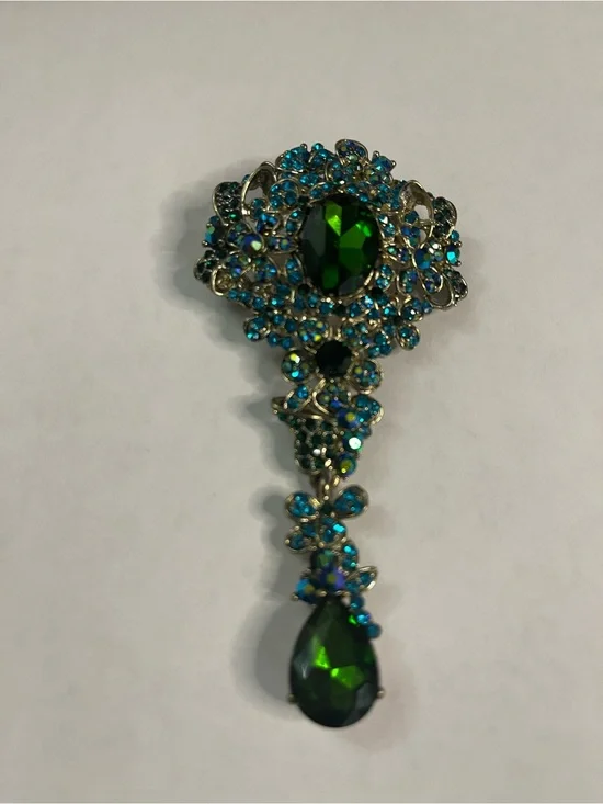 gold-tone teardrop pin featuring a central green crystal surrounded