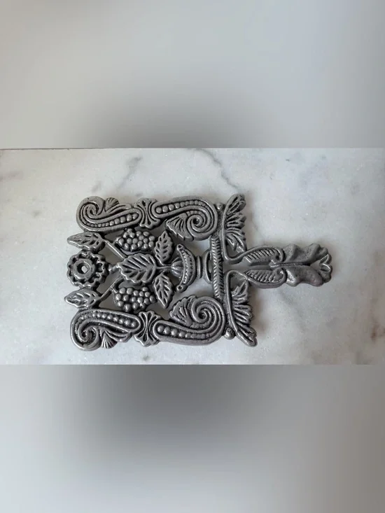 vintage silver-toned metal trivet featuring a decorative design grapes scrolls.