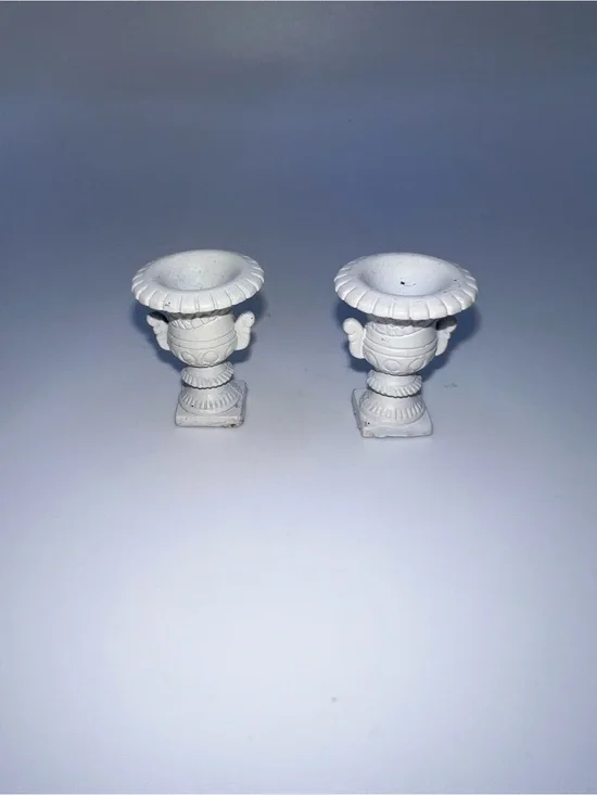Miniature Medici-style vases feature a classic white finish and ornate pedestal